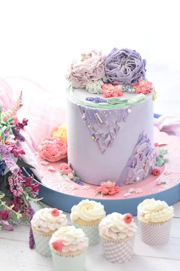 Lavender and pink floral baby shower cake with buttercream blooms, served with matching cupcakes