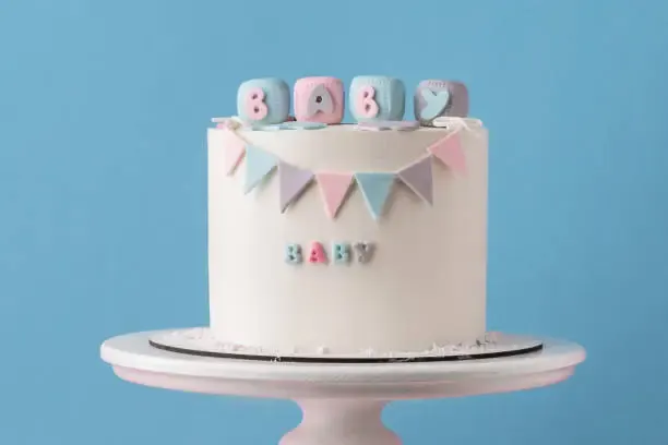White gender reveal baby shower cake with pastel bunting and letter blocks spelling BABY