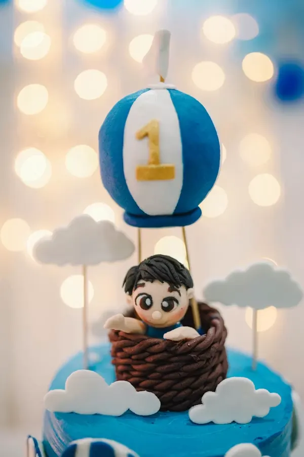 Blue hot air balloon baby shower cake with a fondant baby in a basket and fondant clouds