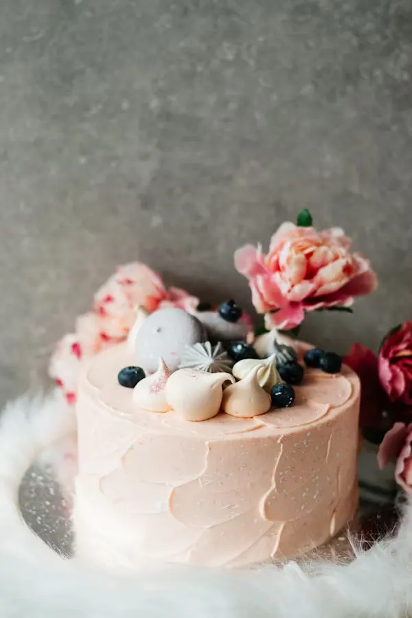Soft pink minimalist baby shower cake topped with meringues, blueberries and fresh peonies