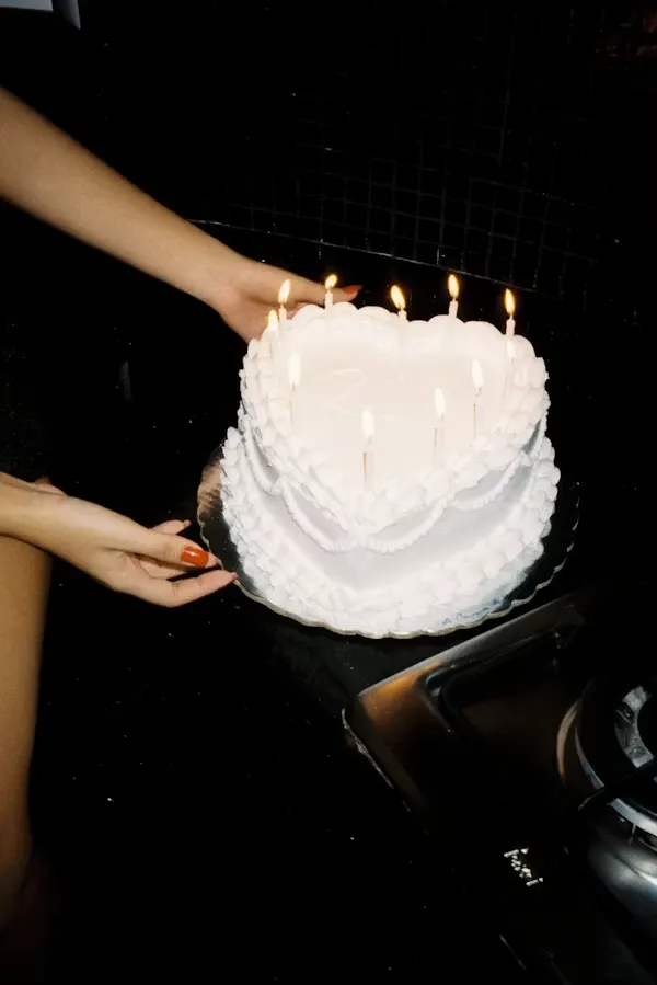 White heart-shaped cake with ruffled buttercream piping and lit candles