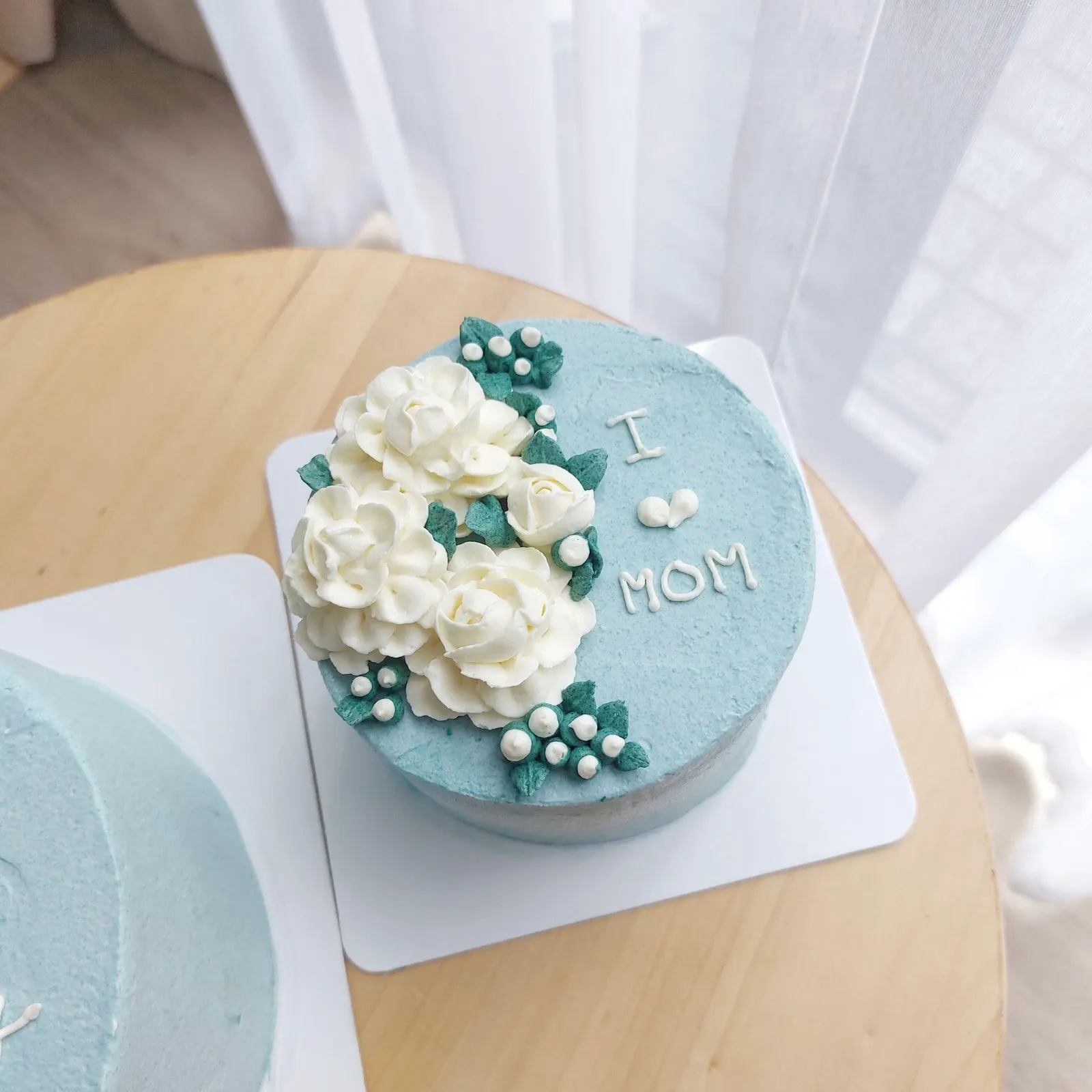 Teal buttercream cake topped with white buttercream roses and piped 'I ♥ MOM' lettering