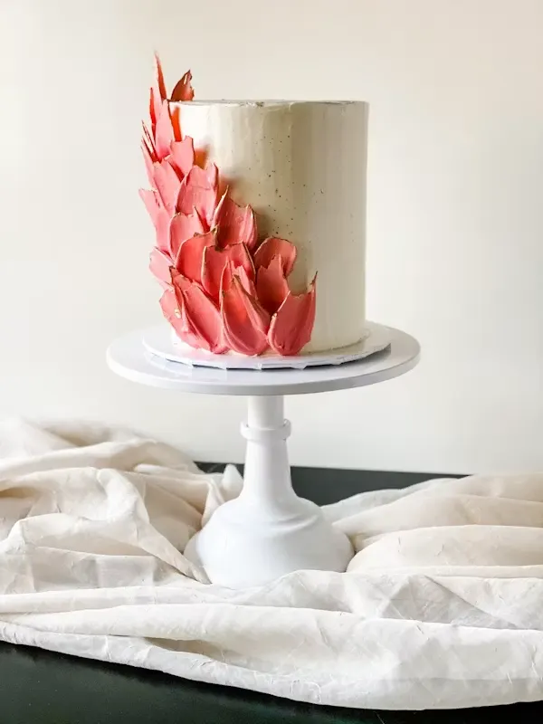 Tall cream buttercream cake with a cascade of coral and gold hand-painted petal detailing down one side