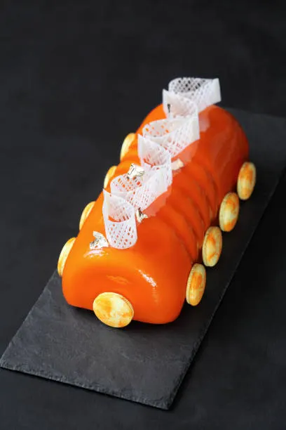 Sculptural orange mirror-glazed entremet log decorated with lace tuile and gold-dusted tartlets