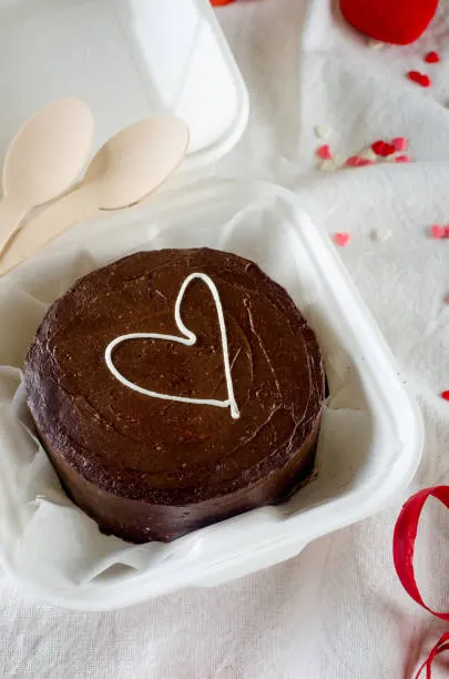 Chocolate bento cake with a piped white heart, wooden spoons and scattered petals beside the box