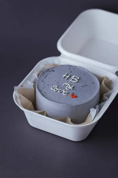 Grey bento cake piped with HB my love in white script and a small red heart, in an open box against a dark background