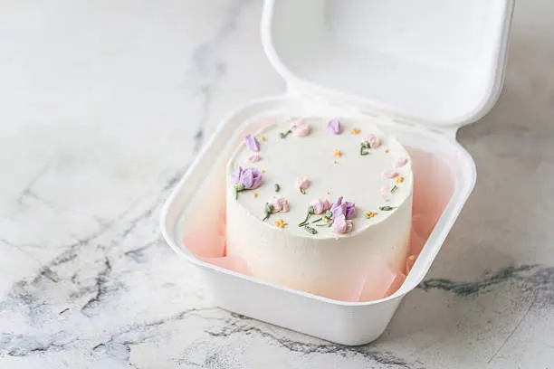 White bento cake decorated with delicate pastel purple and pink flowers on a marble surface