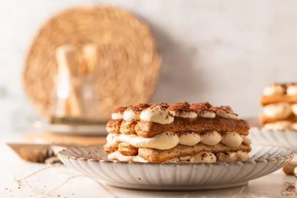 Classic layered tiramisu slice dusted with cocoa on a grey plate