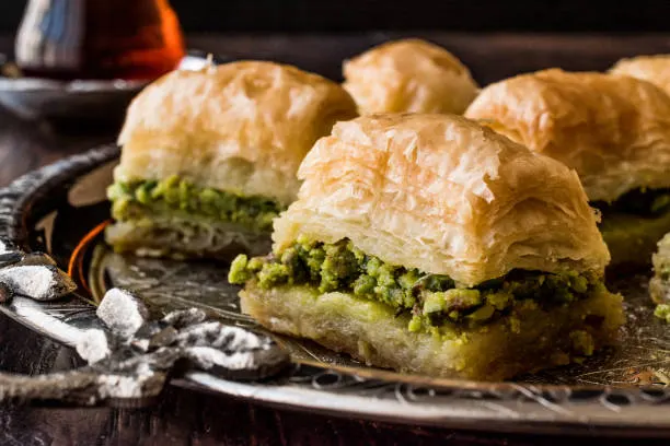 Close-up of golden baklava pieces with pistachio filling on a silver tray